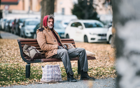 Homeless beggar man with a bag sitting on bench outdoors in city. Copy space.の写真素材