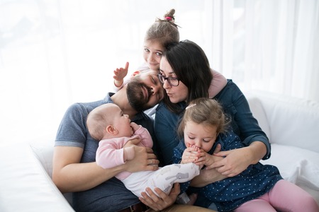 A portrait of young family with small children sitting indoors on a sofa, having fun.の写真素材