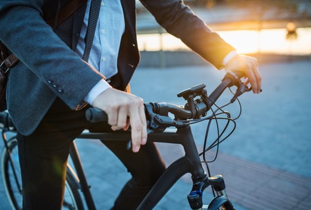 Midsection of businessman commuter with electric bicycle traveling from work in city.