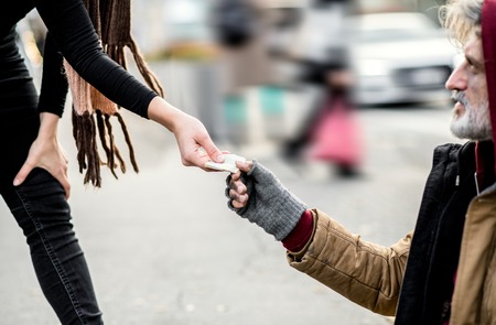 A midsection of woman giving money to homeless beggar man sitting in city.の写真素材
