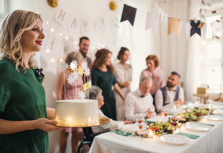 A young woman holding a birthday cake on an indoor party.の写真素材