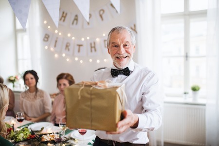 A senior man holding a present in a box on a indoor family birthday party.