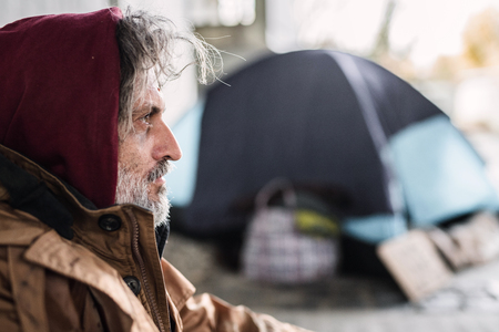 A side view portrait of homeless beggar man sitting outdoors. Copy space.