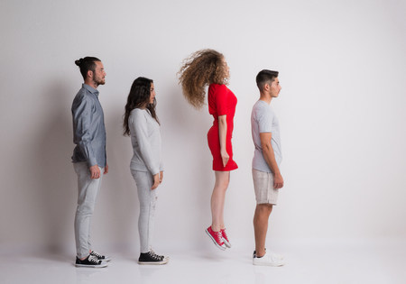Side view of young group of friends standing in a studio, one is jumping.の写真素材