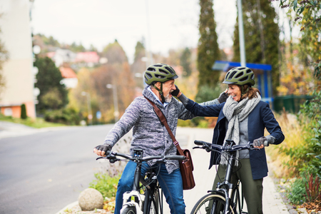 Active senior people with electrobikes greeting outdoors on a road in town.の写真素材