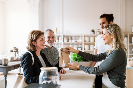 Senior couple buying groceries in zero waste shop, sales assistants serving them.の写真素材