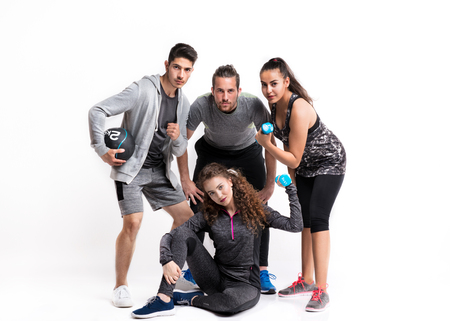 Portrait of joyful young friends with dumbbells standing in a studio.の写真素材