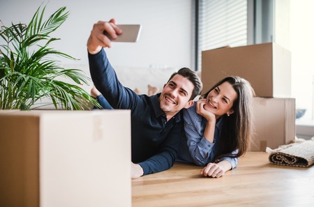 A young couple with a smartphone moving in a new home, taking selfie.の写真素材