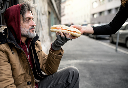 Unrecognizable woman giving food to homeless beggar man sitting in city.の写真素材