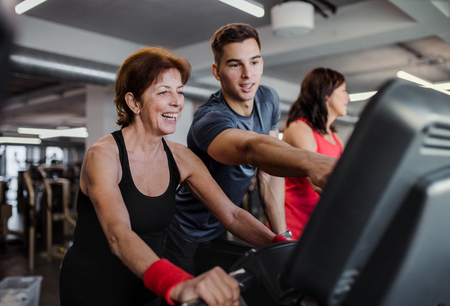 Two cheerful female seniors in gym with a young trainer doing cardio work out.の写真素材