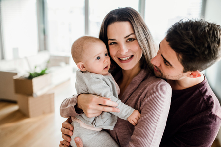 A portrait of young couple with a baby and cardboard boxes moving in a new home.