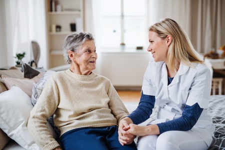 A health visitor talking to a sick senior woman sitting on bed at home.の写真素材