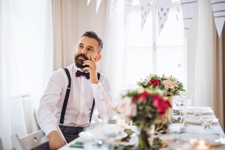 A portrait of a thoughtful mature man sitting indoors in a room set for a party.の写真素材