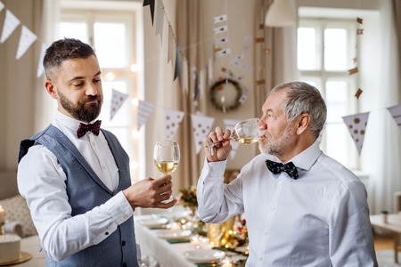 Senior and mature man standing indoors in a room set for a party, degusting wine.の写真素材