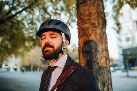 Businessman commuter with helmet standing in city at sunset, eyes closed.の写真素材