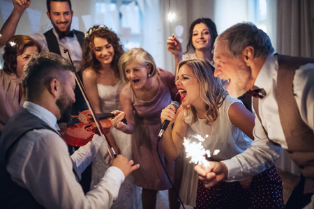 A young bride, groom and other guests dancing and singing on a wedding reception.の写真素材