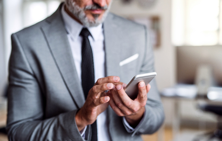 A midsection of businessman standing in an office, using smartphone.の写真素材