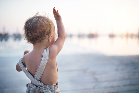 A rear view of small toddler girl standing on beach on summer holiday.の写真素材