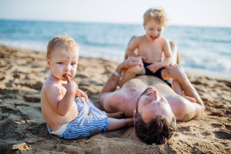 A father with two toddler children lying on sand beach on summer holiday.の写真素材