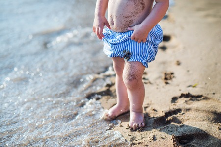 A midsection of small toddler girl with shorts walking on sand beach on holiday.の写真素材