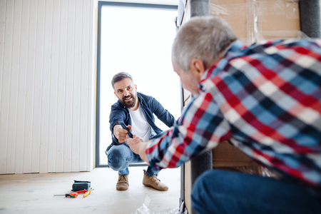 A senior man helping his son with furnishing new house, a new home concept.の写真素材