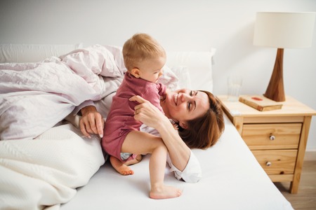 A young mother with little daughter sitting indoors on bed in the morning, playing.の写真素材