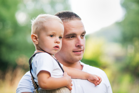 Young father holding a small toddler son in sunny summer nature.の写真素材