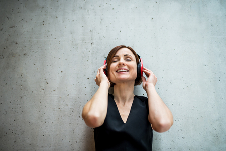 Young business woman with headphones standing against concrete wall in office.の写真素材
