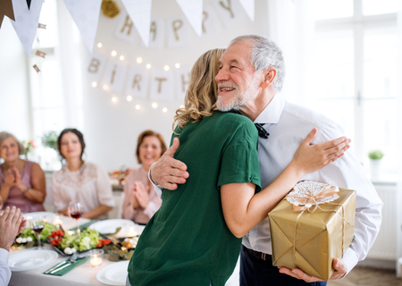 Young woman giving a gift to her grandfather on indoor party, hugging.の写真素材