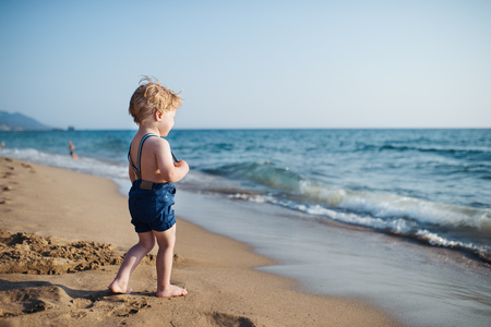 A small toddler boy with shorts walking on sand beach on summer holiday.の写真素材