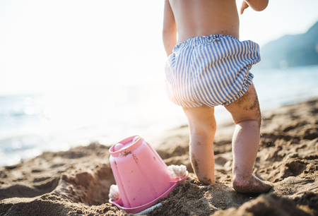 A midsection of small toddler girl with shorts playing on sand beach on holiday.の写真素材