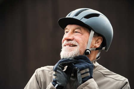 An active senior man standing outdoors in town, putting on a bike helmet.の写真素材