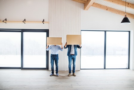 Two men holding cardboard boxes in front of their head when furnishing new house.の写真素材