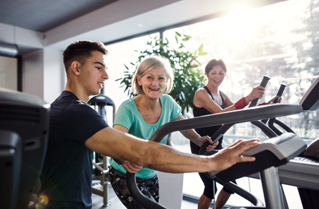 Two cheerful female seniors in gym with a young trainer doing cardio work out.の写真素材
