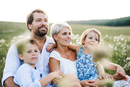 Young family with small children in summer nature at sunset, sitting in the grass.の写真素材