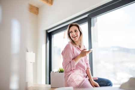 A young woman with smartphone moving in new home, sitting on table.の写真素材
