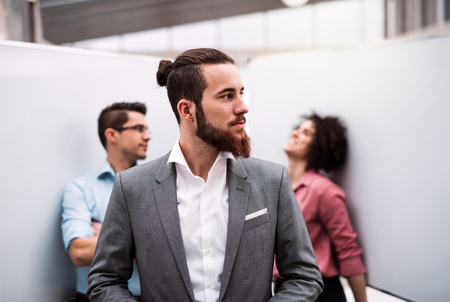 A young businessman in suit standing in office, colleagues in the background.の写真素材