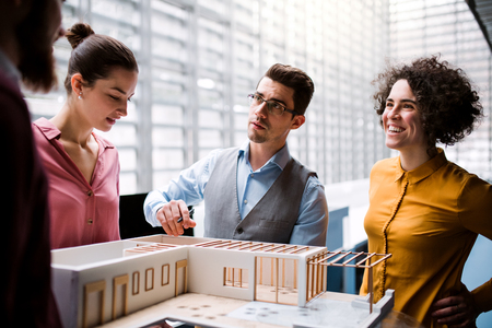 Group of young architects with model of a house standing in office, talking.の写真素材