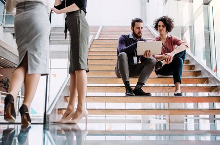 Group of young businesspeople stitting on a staircase, talking.