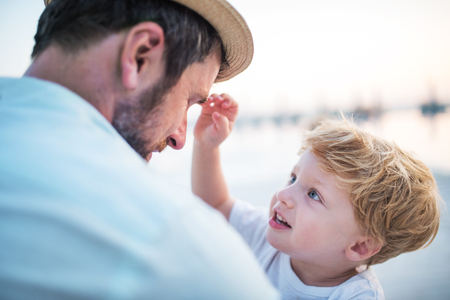 A father holding a toddler boy on beach on summer holiday.の写真素材