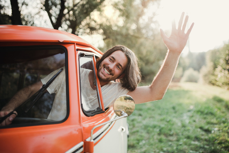 A young man driver in a car on a roadtrip through countryside, waving.の写真素材