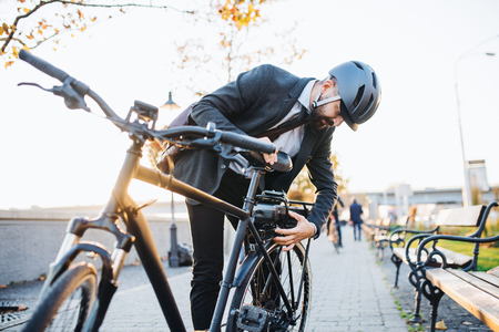 Hipster businessman commuter setting up electric bicycle in city.の写真素材