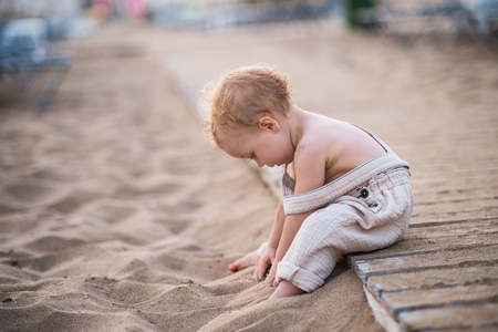 A small toddler girl sitting on beach on summer holiday, playing.の写真素材