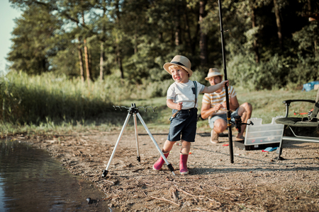 A mature father with a small toddler son outdoors fishing by a lake.の写真素材