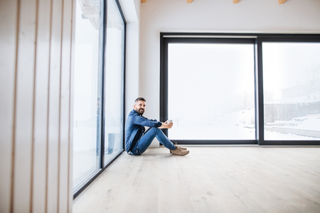 A mature man sitting on the floor in unfurnished new house, holding coffee.の写真素材