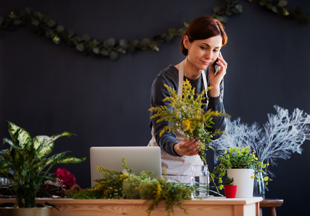 Young creative woman in a flower shop, using smartphone. A startup of florist business.の写真素材