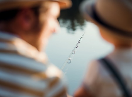 A rear view of mature father with a small toddler son outdoors fishing by a lake.の写真素材