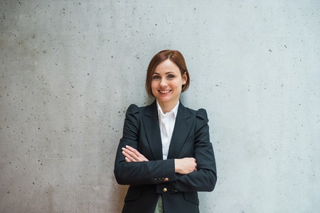 A portrait of young businesswoman standing in office, looking at camera.