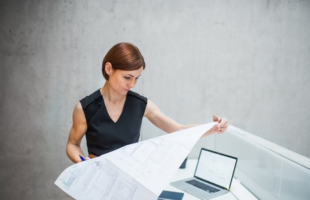 Young businesswoman or architect with blueprints standing in office.の写真素材