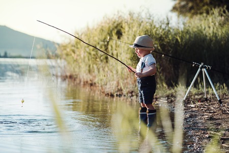 A small toddler boy standing by a lake at sunset, fishing. Copy space.の写真素材